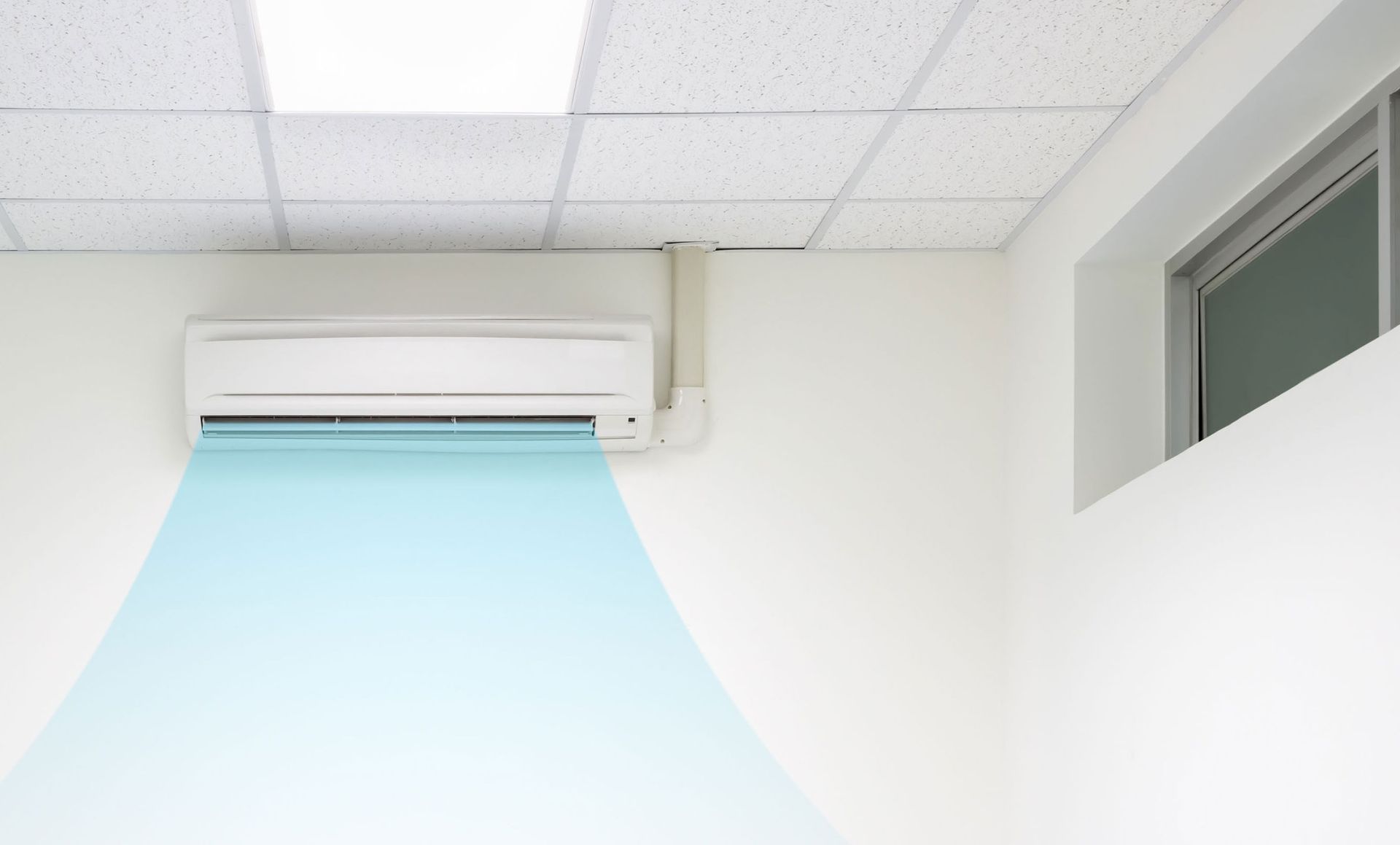Wall-mounted air conditioner blowing cool blue air in a bright office room