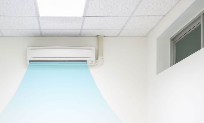 Wall-mounted air conditioner blowing cool blue air in a bright office room