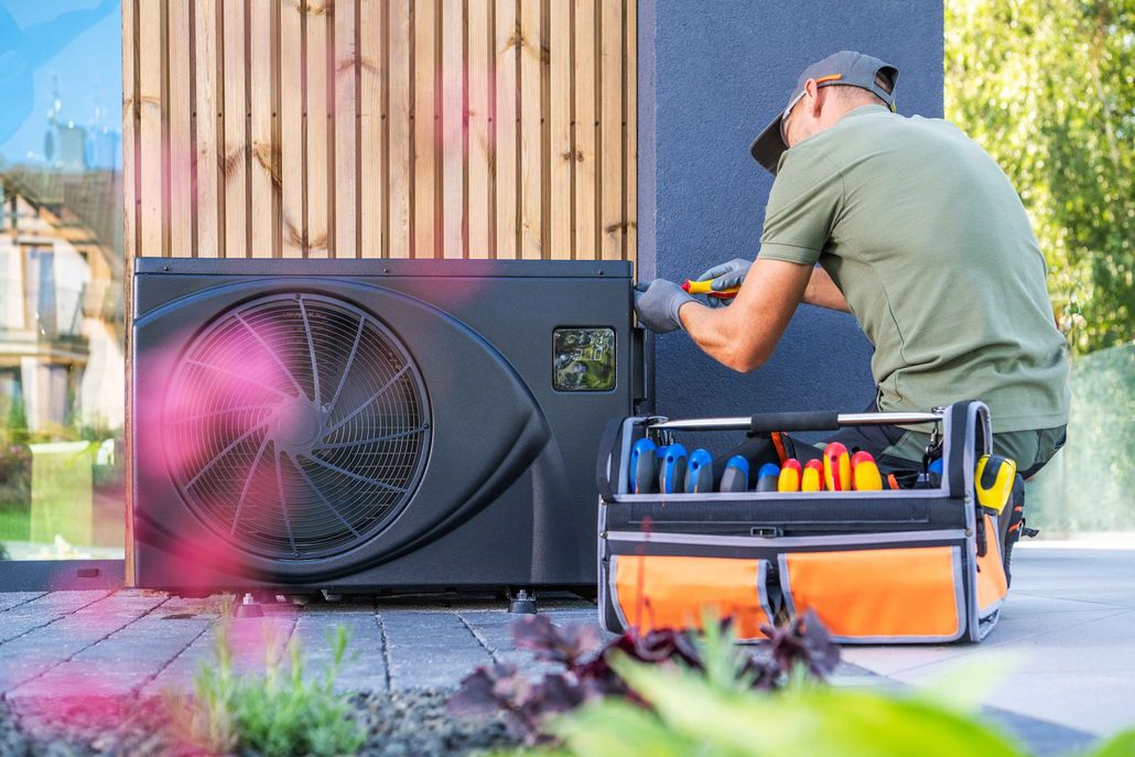 Worker repairing an outdoor HVAC unit beside a toolbox and wooden wall