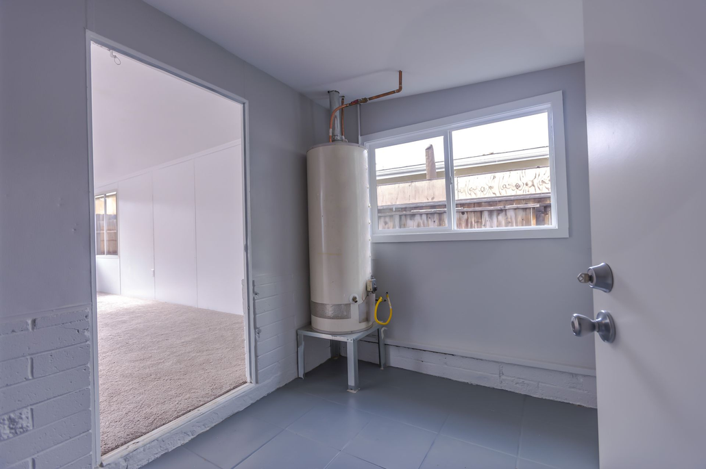 Empty utility room with a water heater, gray walls, and a window.