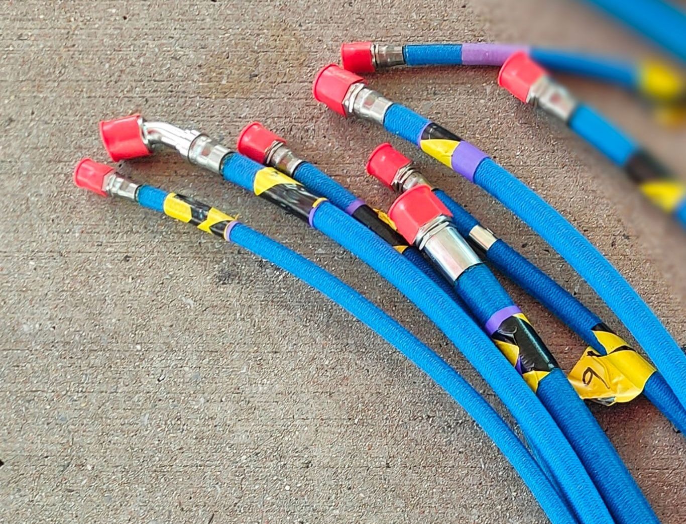 Blue hoses with metal fittings, red caps, and colorful tape, lying on concrete.