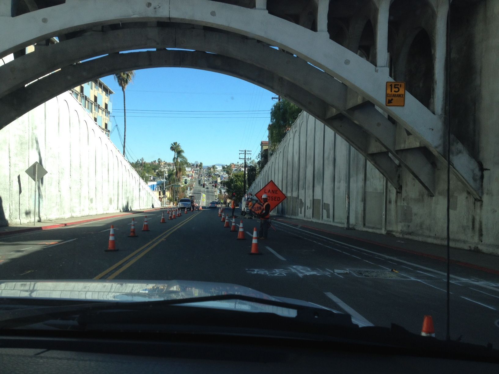 A car is driving under a bridge with cones on the road.