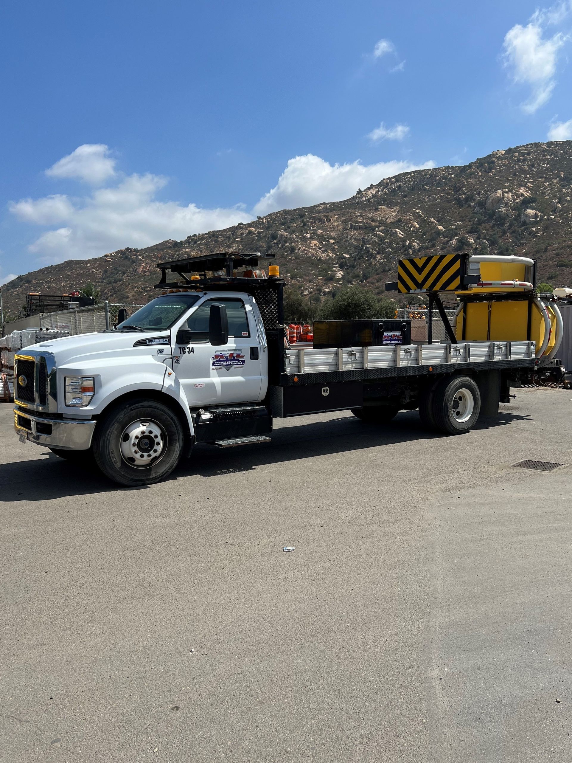 White flatbed tow truck parked on gravel with mountains and blue sky in the background