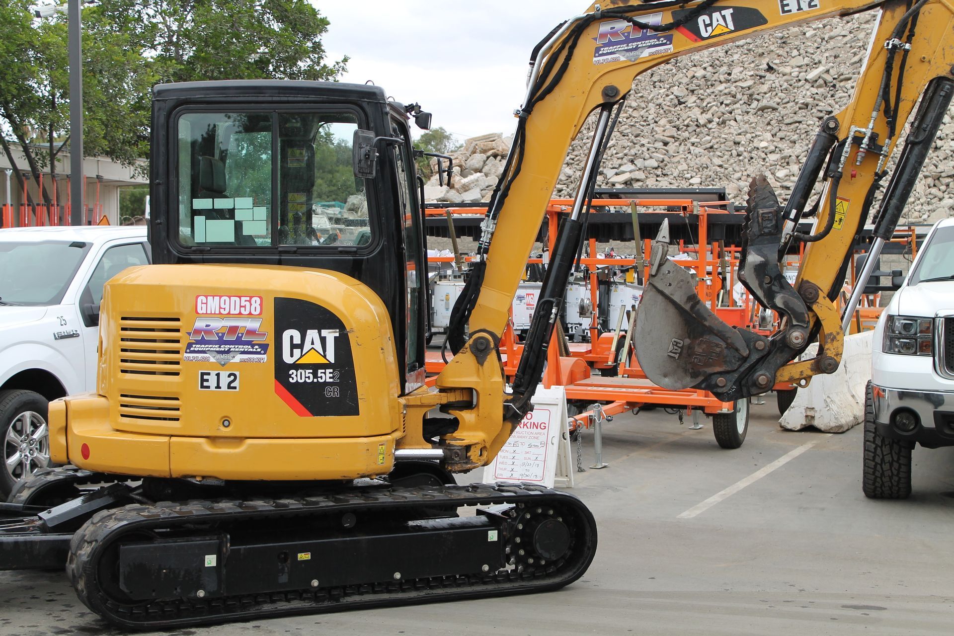 Yellow CAT mini excavator on a city street beside other construction equipment and vehicles
