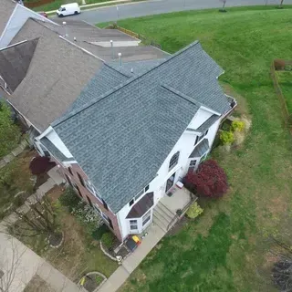 An aerial view of a multi-story home with a grey shingled roof, white siding, and a red brick section next to a grassy lawn.