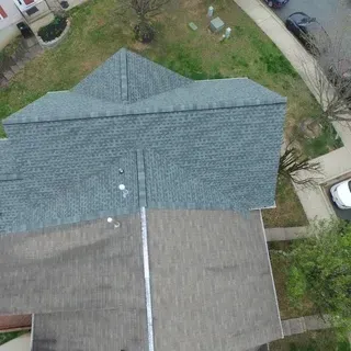 An aerial view of a gray shingled roof with a metal ladder leaning against the ridge line.