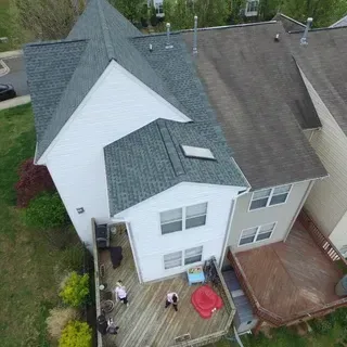 Aerial view of two joined houses with grey shingled roofs and back decks; two people stand on the lower wooden deck.
