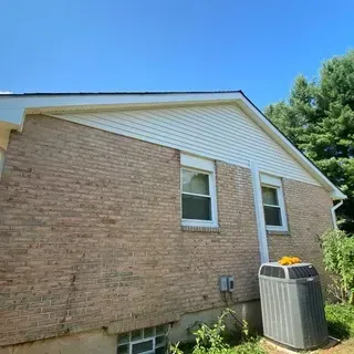 Side exterior of a brick house with white vinyl siding on the gable, two windows, and an air conditioning unit.