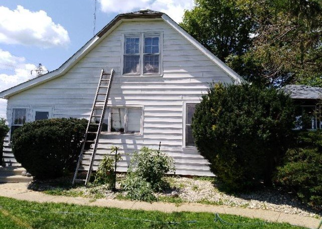 A white, two-story house with horizontal siding and a tall wooden ladder leaning against its exterior wall.