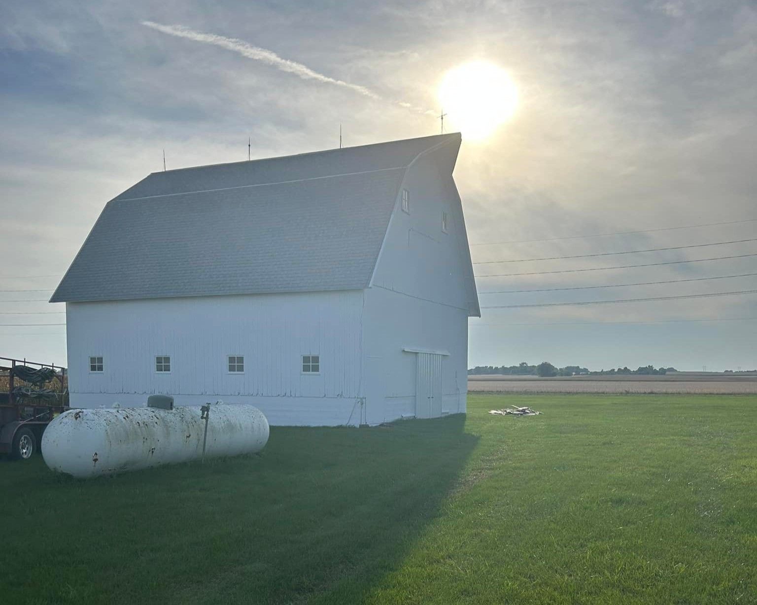 White barn on a green field with two propane tanks. Sun shining brightly in sky.