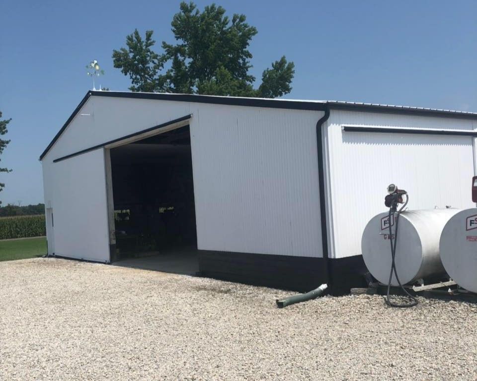 White and black farm building with an open doorway. Two white fuel tanks are on the right.