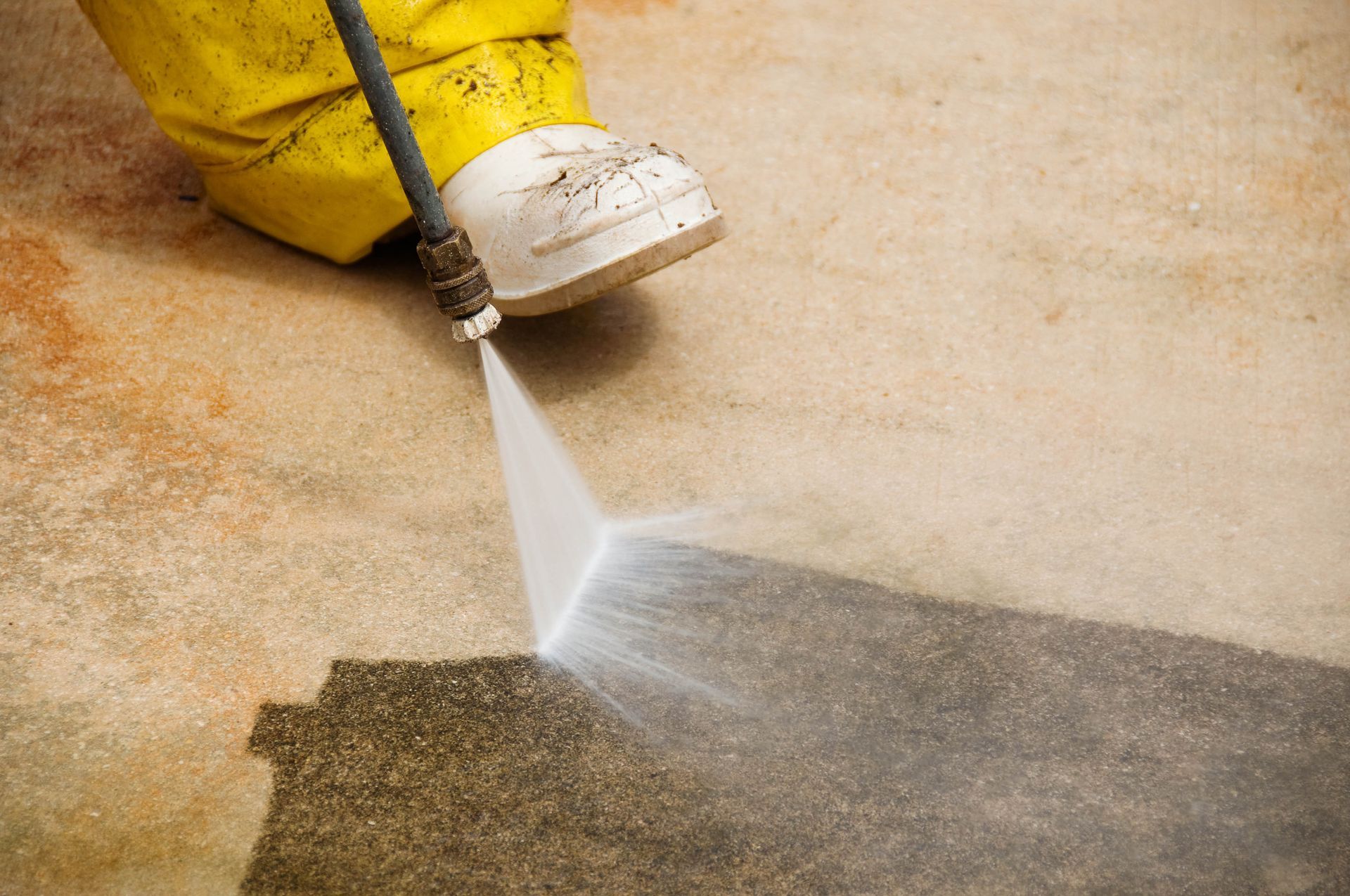 Person pressure washing a dirty concrete surface with water, cleaning a strip.