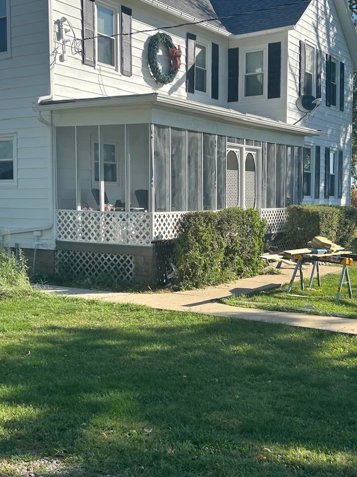 White house with screened porch, green lawn, and Christmas wreath.