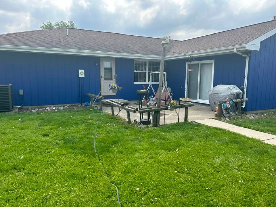 Backyard with blue building, green lawn, patio table, and barbecue grill.