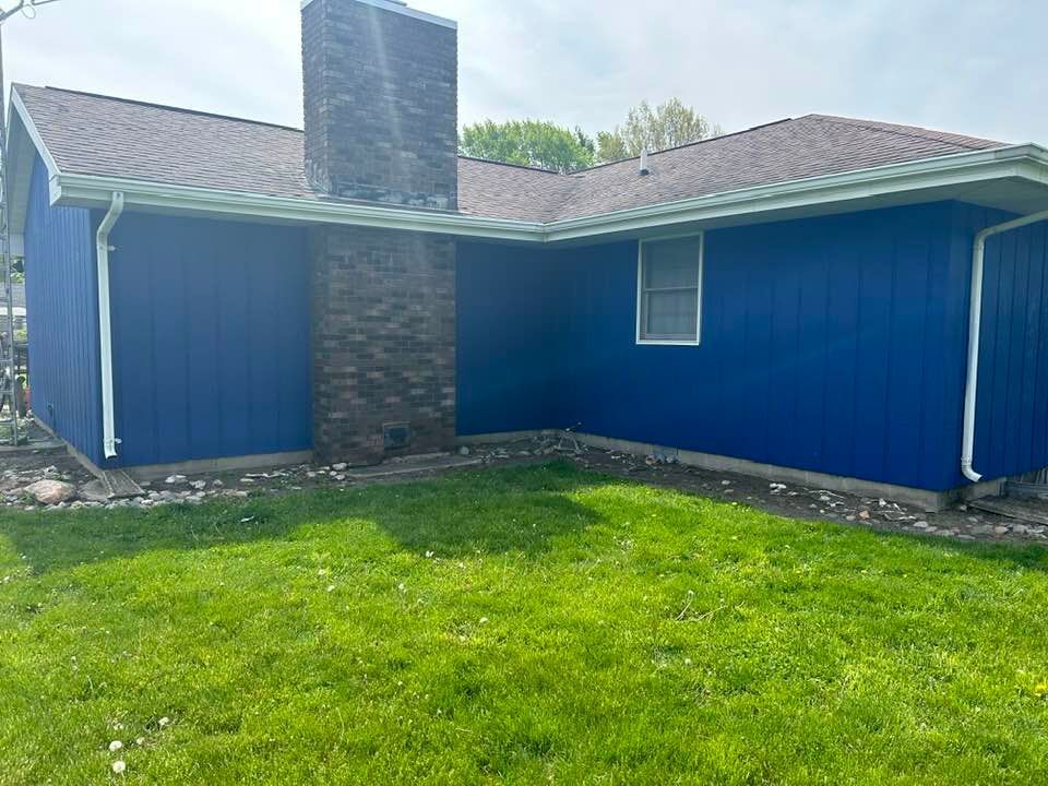 Blue house with a brick chimney, green lawn, and brown roof.