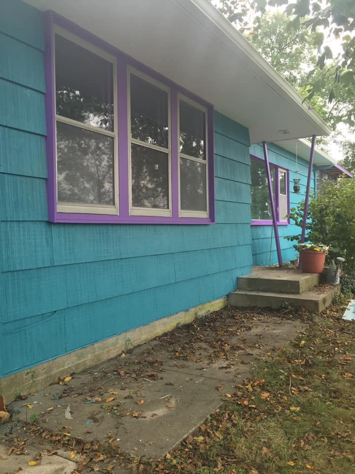 Turquoise house with purple window frames and a concrete pathway.
