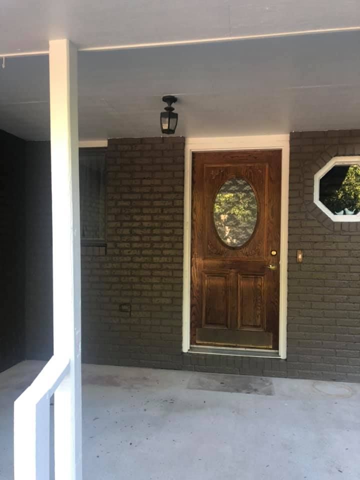 Brown front door with oval glass, on brick wall under a covered porch.