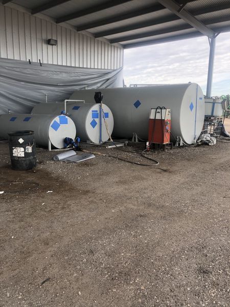 Several large, cylindrical storage tanks with blue hazard symbols under a corrugated metal roof.
