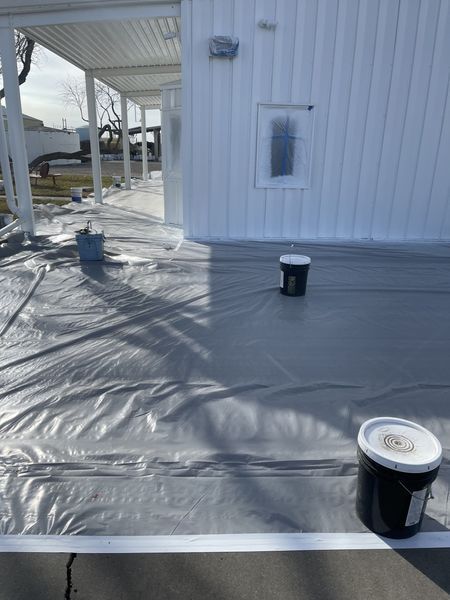 A deck being painted gray with plastic sheeting laid out. Buckets of paint sit nearby the building.