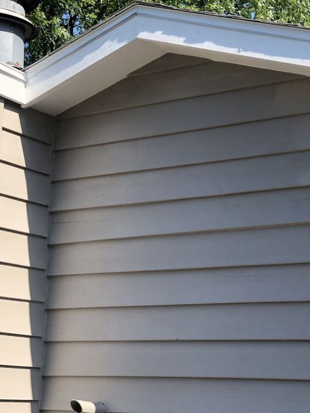 Gray siding on a building with white trim around the roofline, a chimney, and a small pipe.