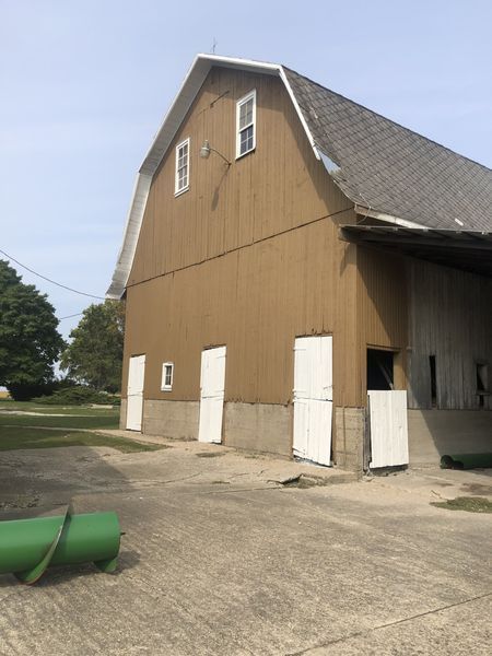 Tan barn with white doors and windows, against a blue sky, on a concrete pad.