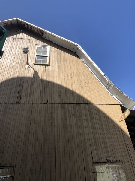 Wooden barn exterior with window and shadow against a blue sky.