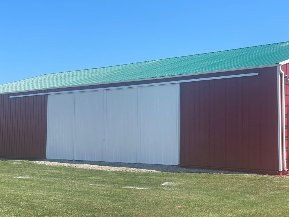 Red barn with white sliding doors, green roof, and blue sky.