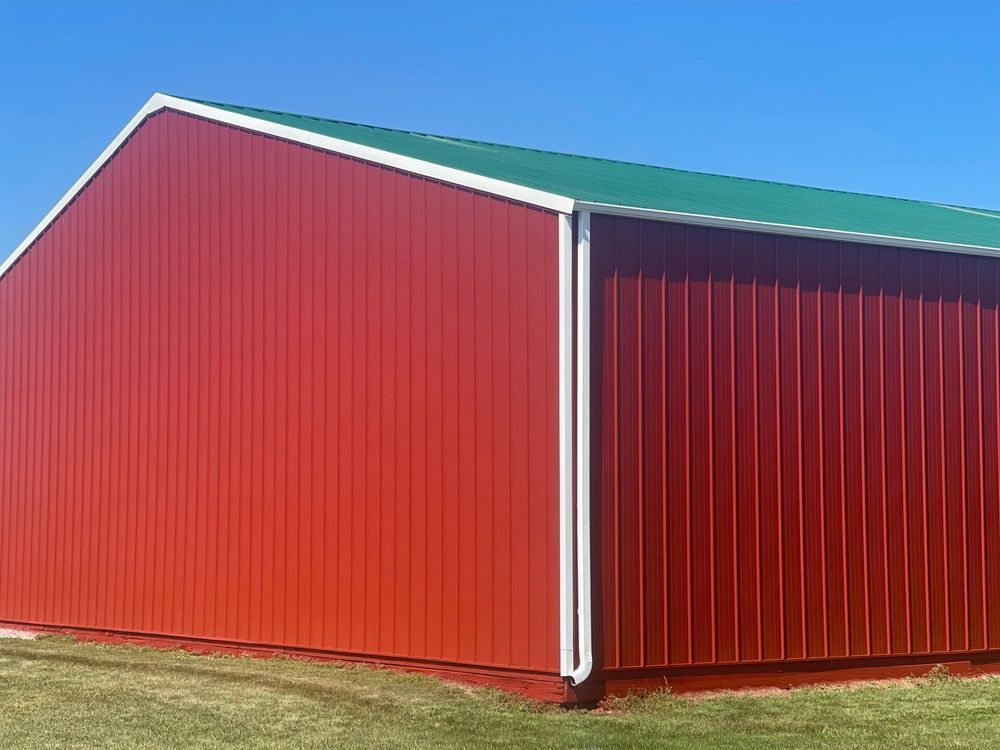 Red metal barn with a green roof against a clear blue sky.