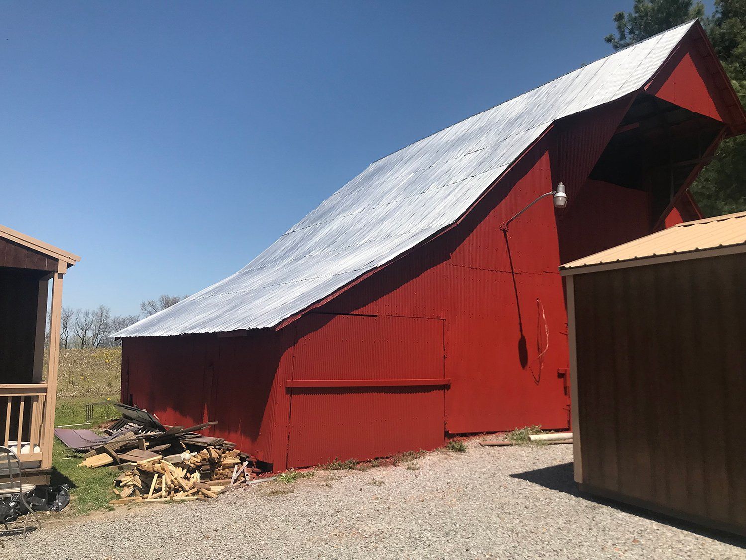 Red barn with a curved roof, a silver metal roof, and a blue sky.