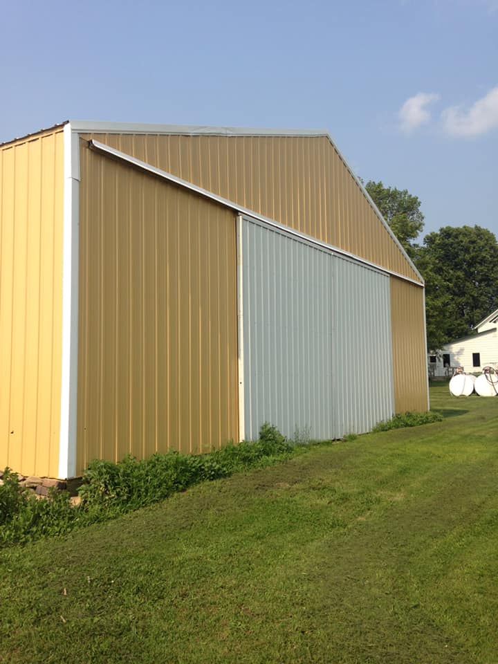 Yellow barn with a white sliding door on a grassy lawn. Blue sky in the background.