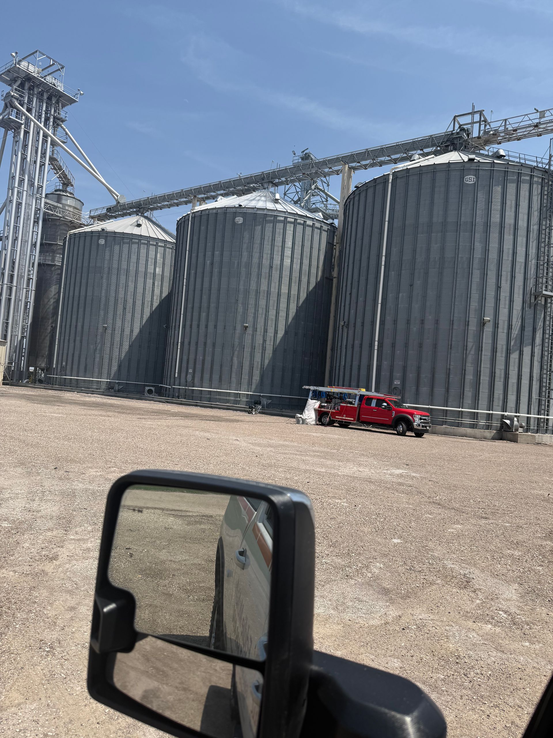 Grain silos stand tall under a blue sky, with a red truck parked in front.