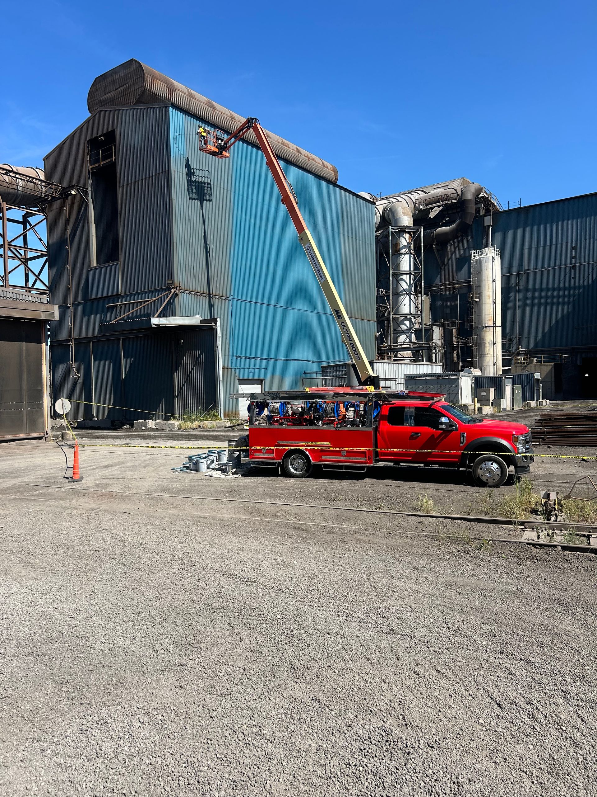 Red fire truck with extended ladder at a damaged industrial building; blue metal siding, smoke, debris.