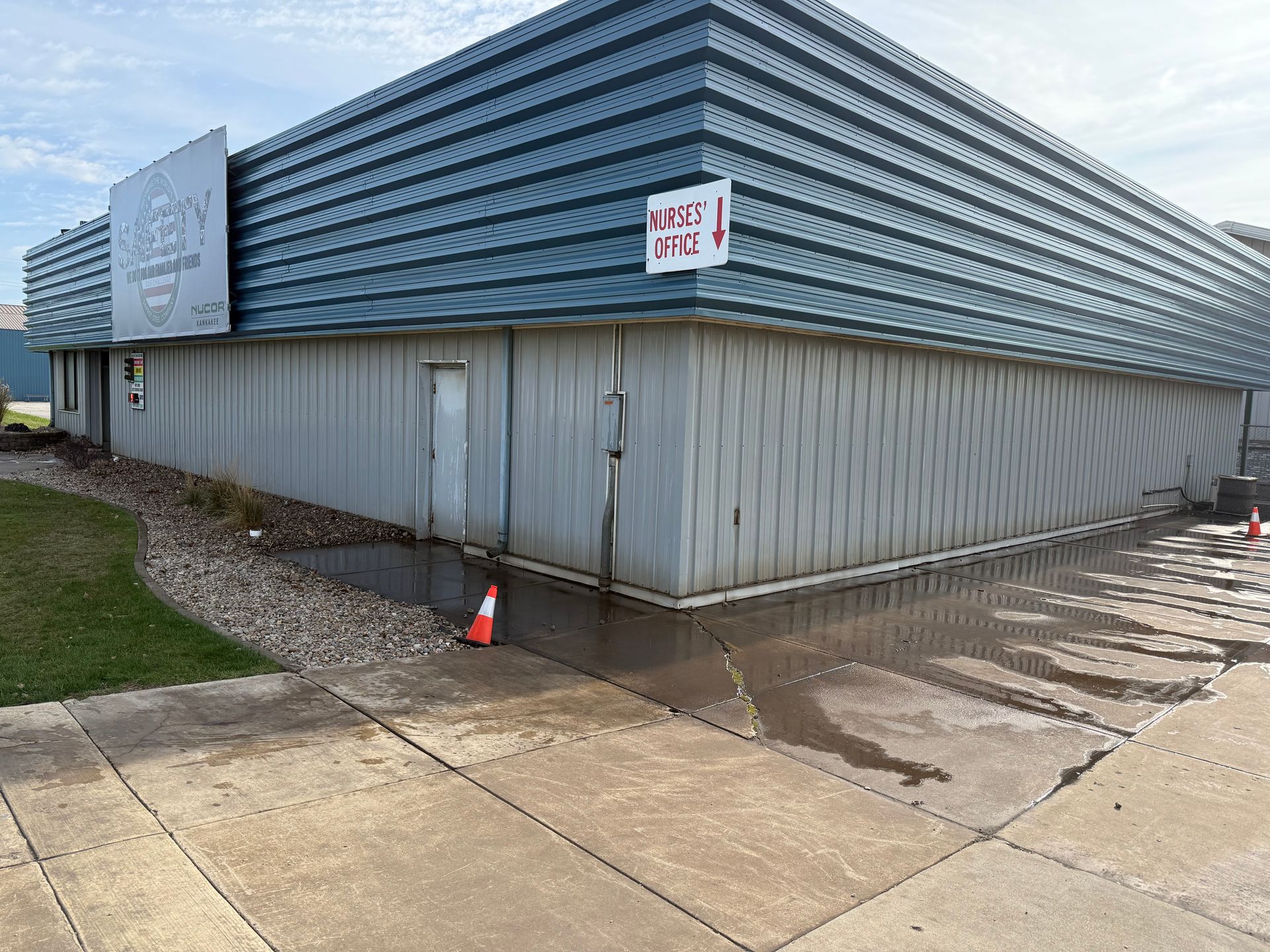 Exterior corner of a building with water damage and pooling water on the ground; a sign says