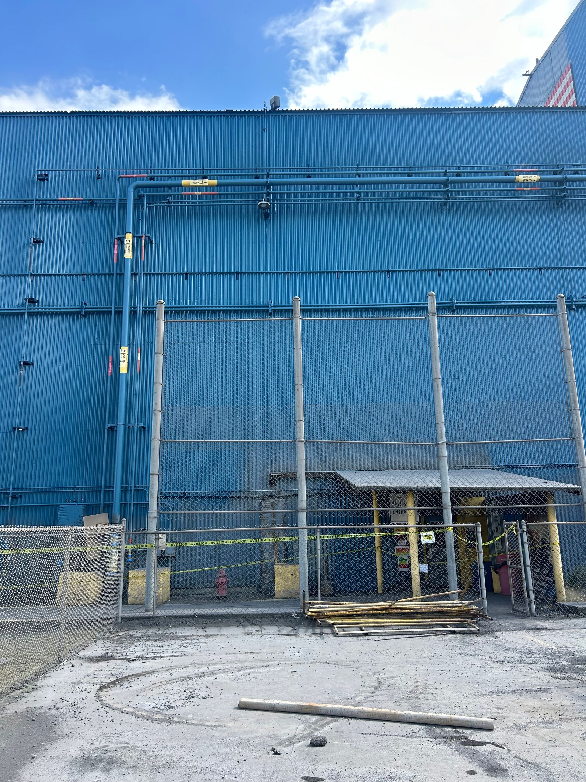 Blue building with a gray fence. Construction area with yellow caution tape and wooden planks.