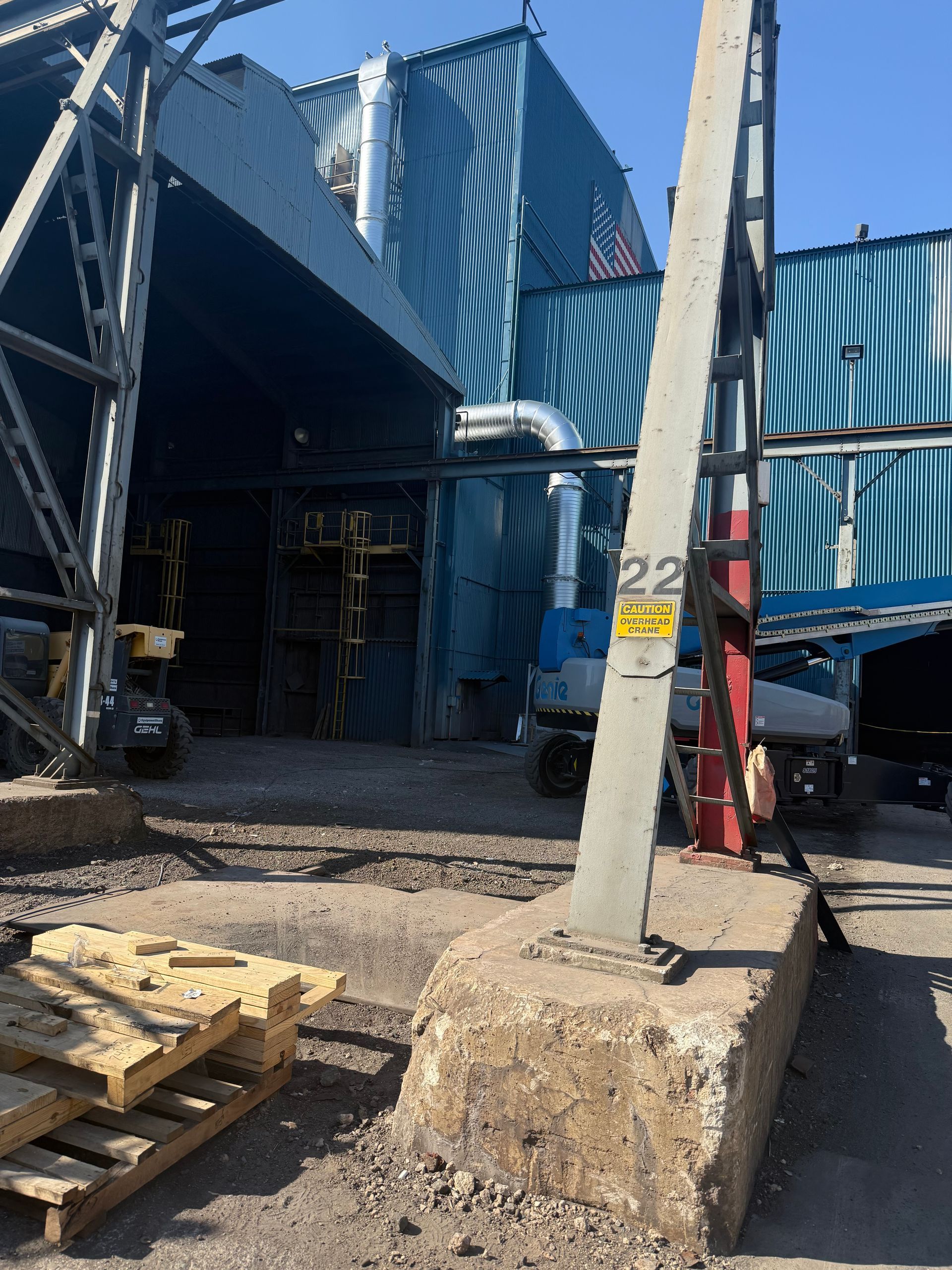 Industrial scene: a blue building with metal supports, a concrete base, and construction equipment in view.