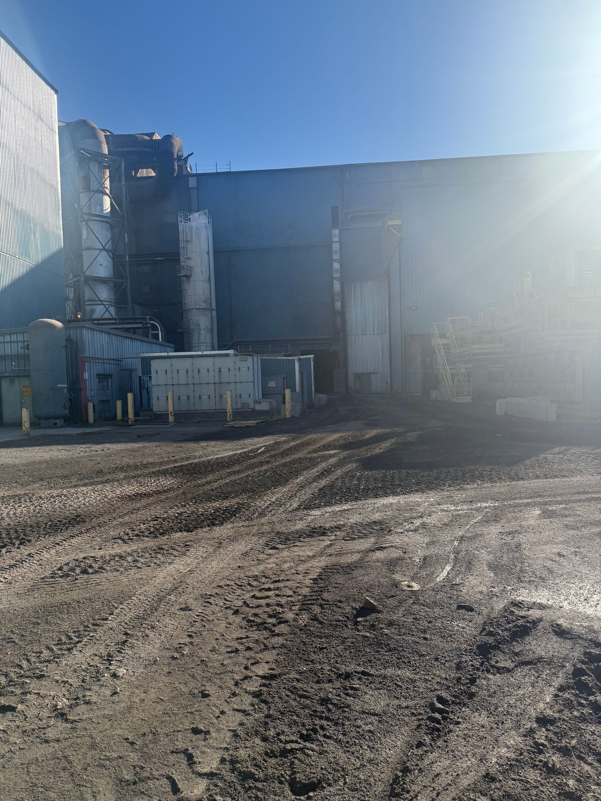 Industrial complex on a dirt lot under a bright, sunny sky.