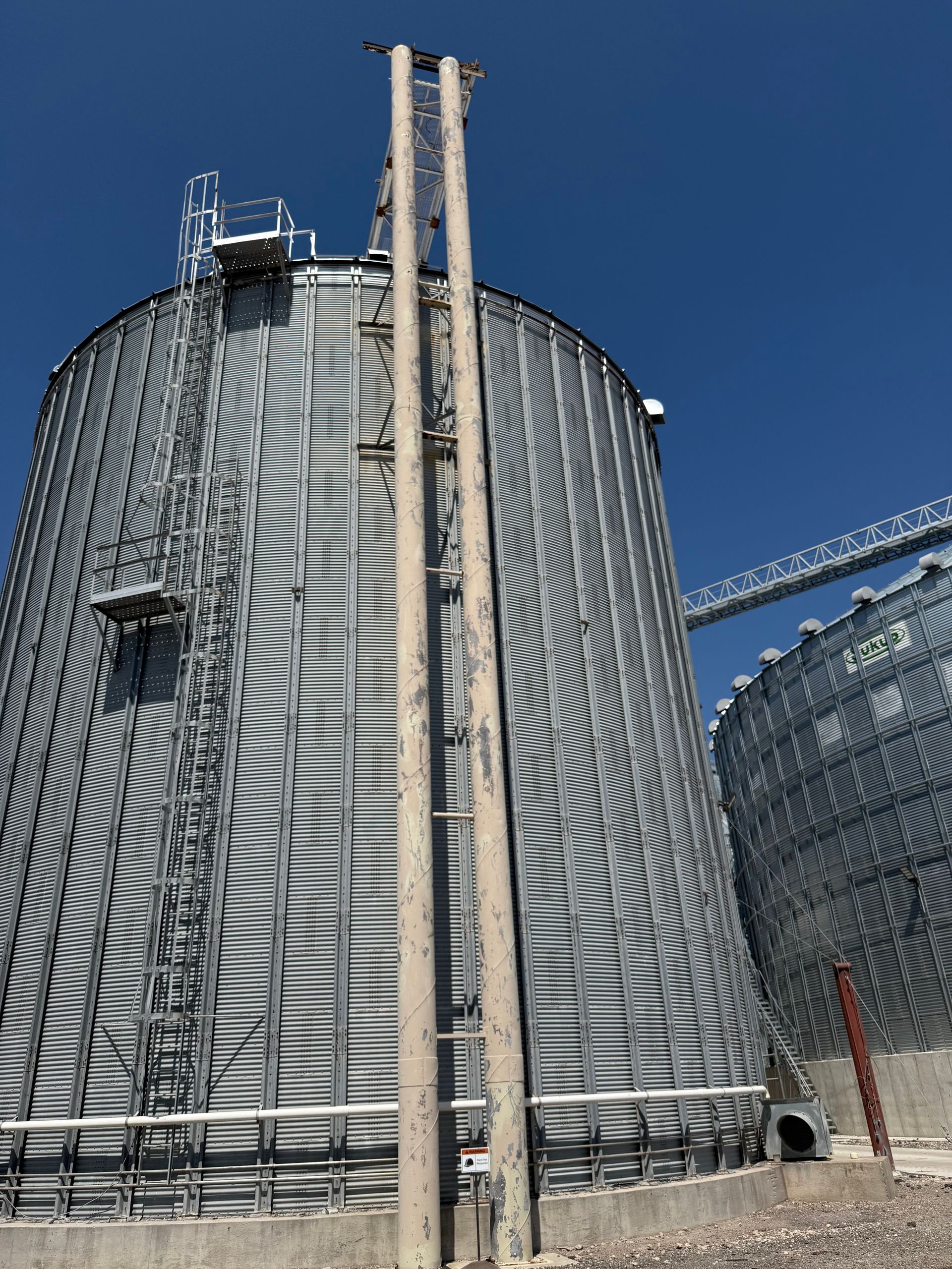 Two large corrugated metal grain silos stand against a clear blue sky.