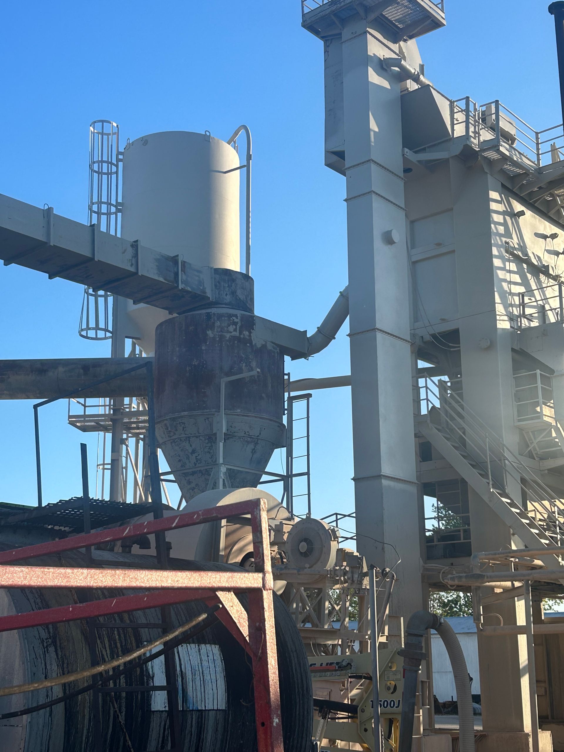 Industrial machinery, including tall silos and metal chutes, stands against a clear blue sky.