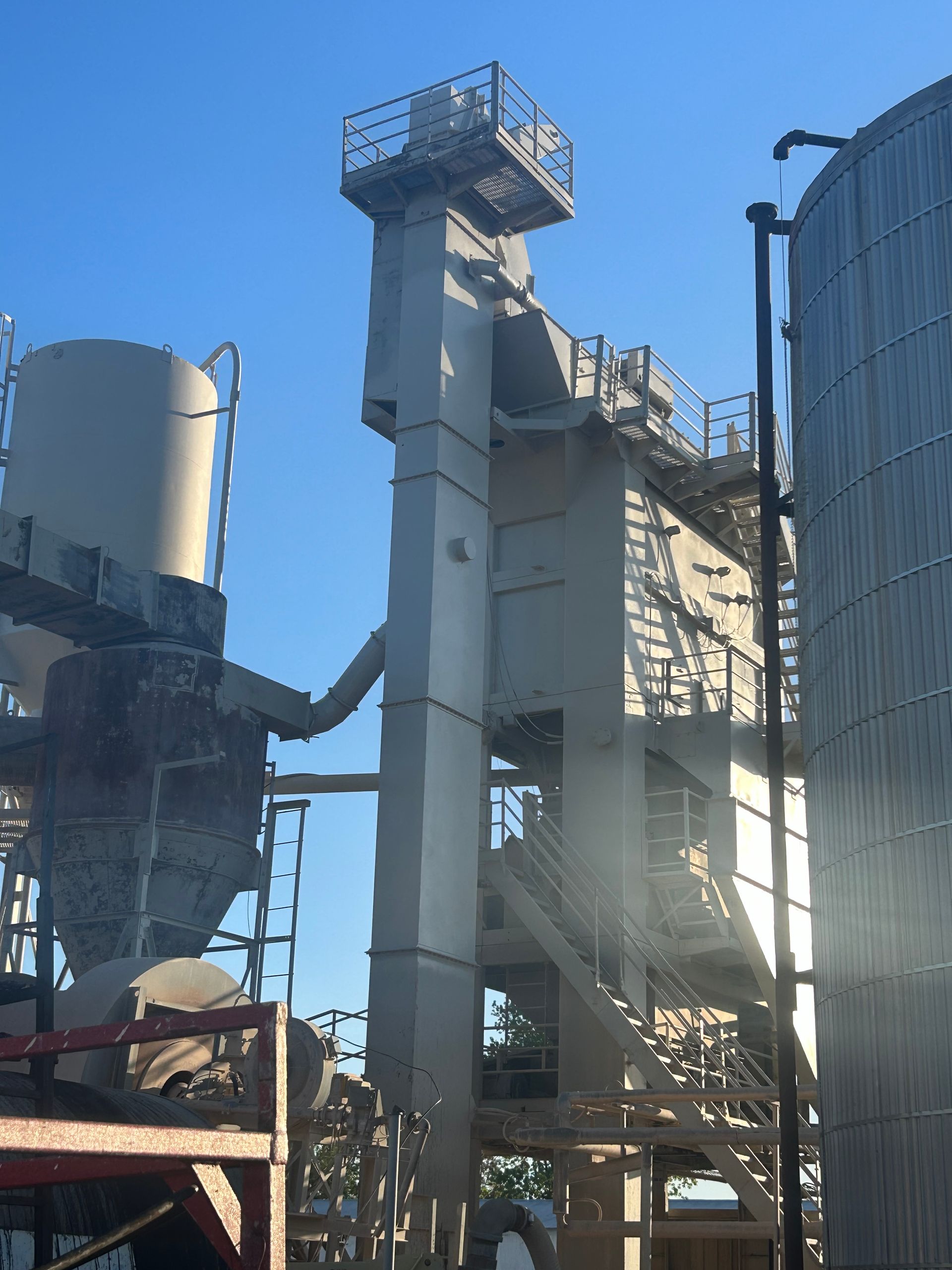 A tall industrial concrete silo structure with a metal elevator shaft against a clear blue sky.