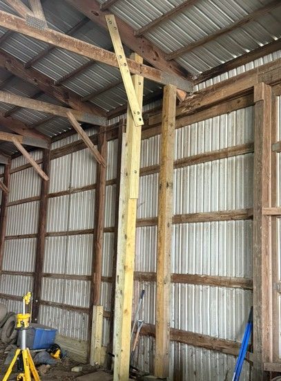 A wooden support post braced with an angled board inside a metal-sided pole barn.
