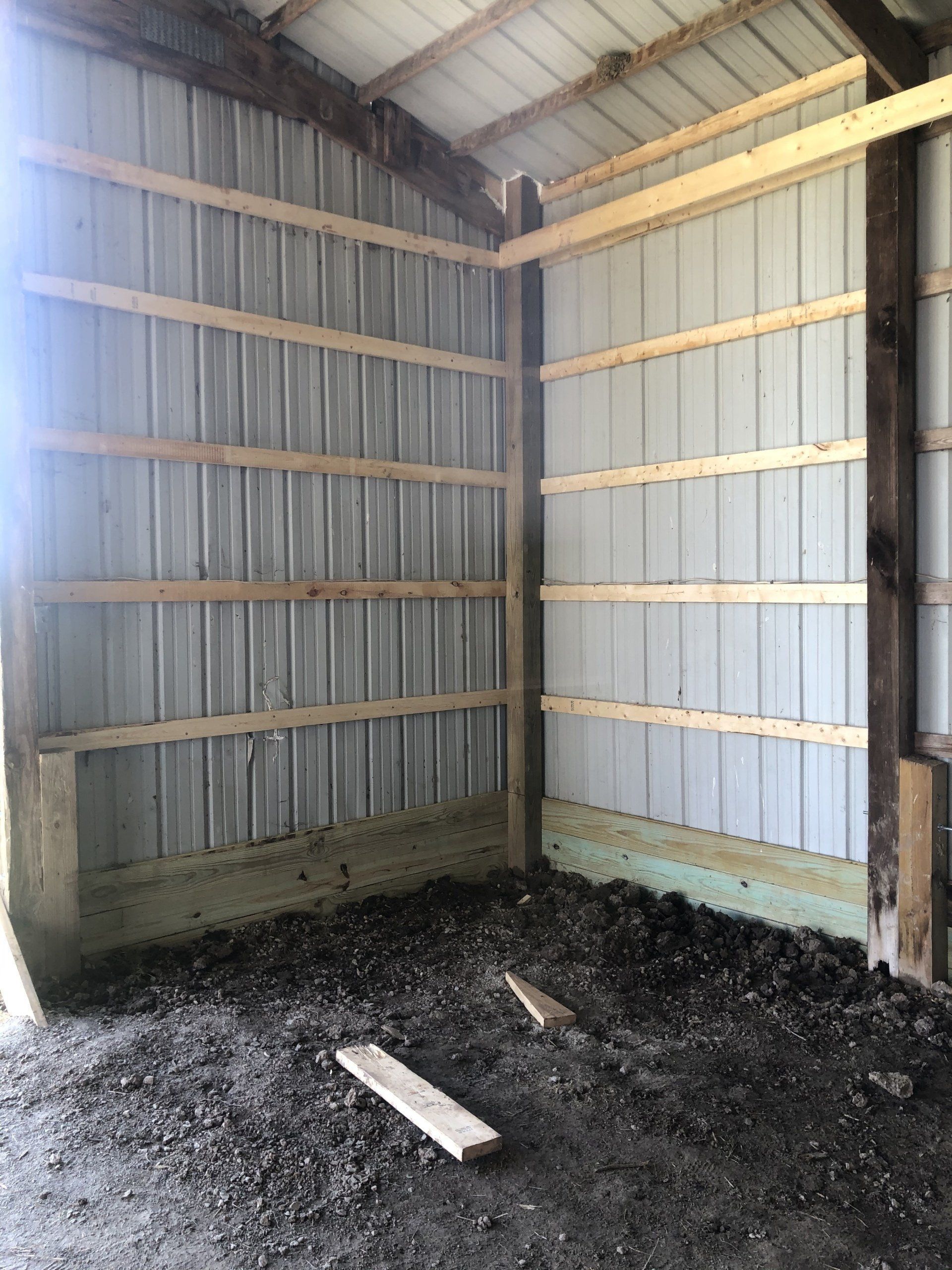 Interior corner of a metal-sided pole barn with exposed wood framing and a dirt floor.
