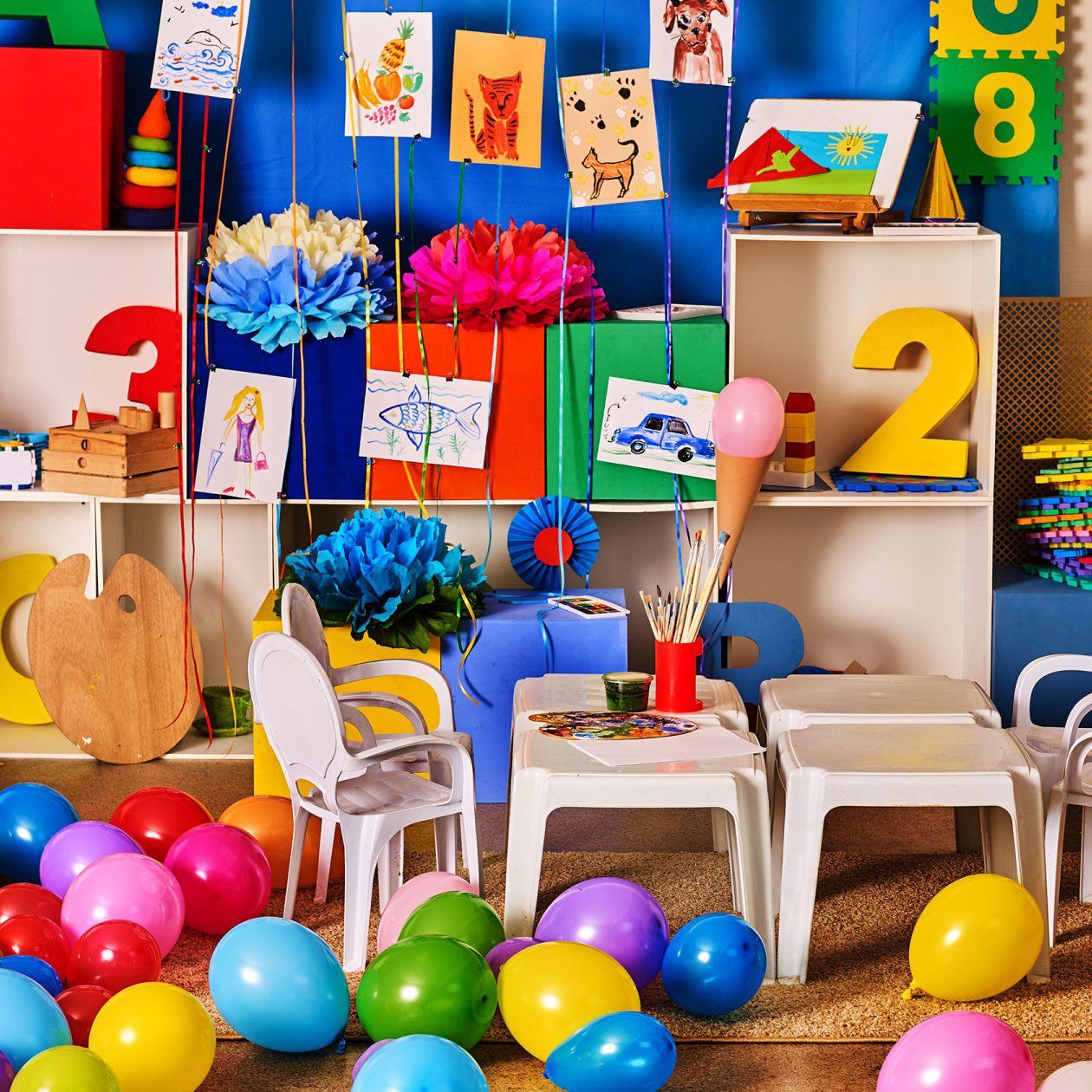 A colorful playroom with balloons, artwork, small tables, and chairs, decorated for a child's birthday.