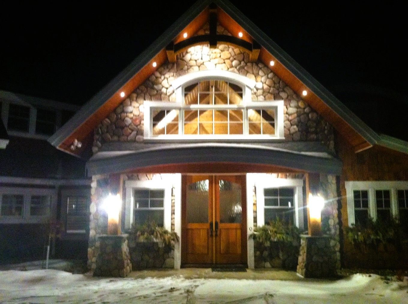 Illuminated wooden house entrance at night with peaked roof and double doors