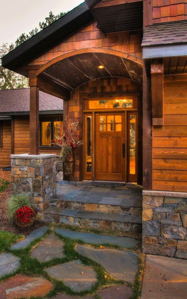 Wooden front entrance with stone steps and porch, warmly lit at dusk