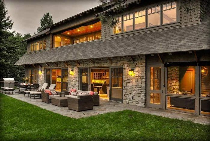 Stone house with warm lit windows, patio seating, and an outdoor fire pit at dusk