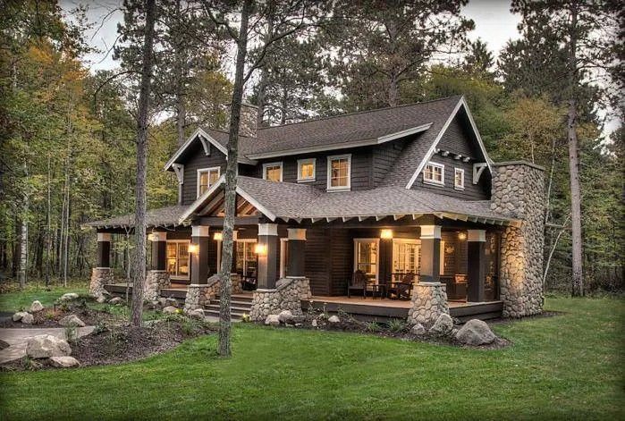 Cozy stone-and-wood cabin with lit windows and porch lights in a wooded forest setting at dusk