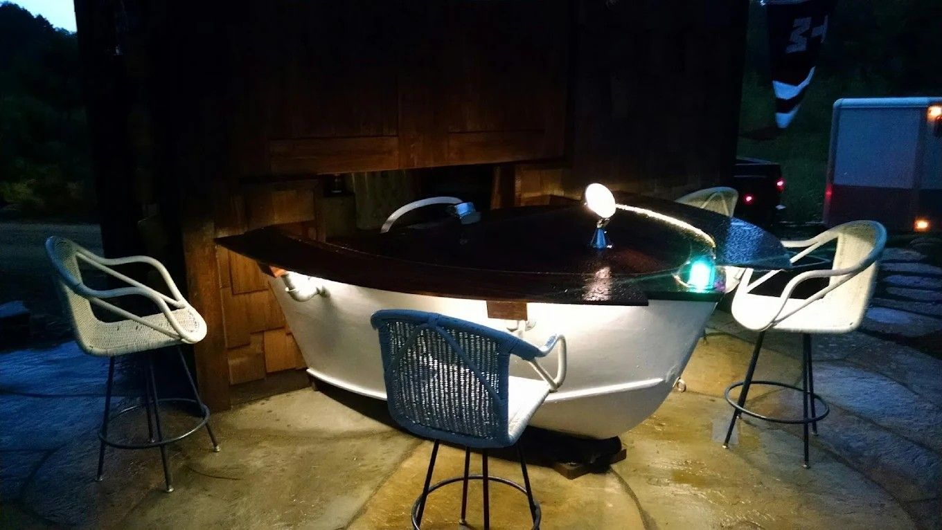 Outdoor white hot tub surrounded by four chairs on a dimly lit patio at night