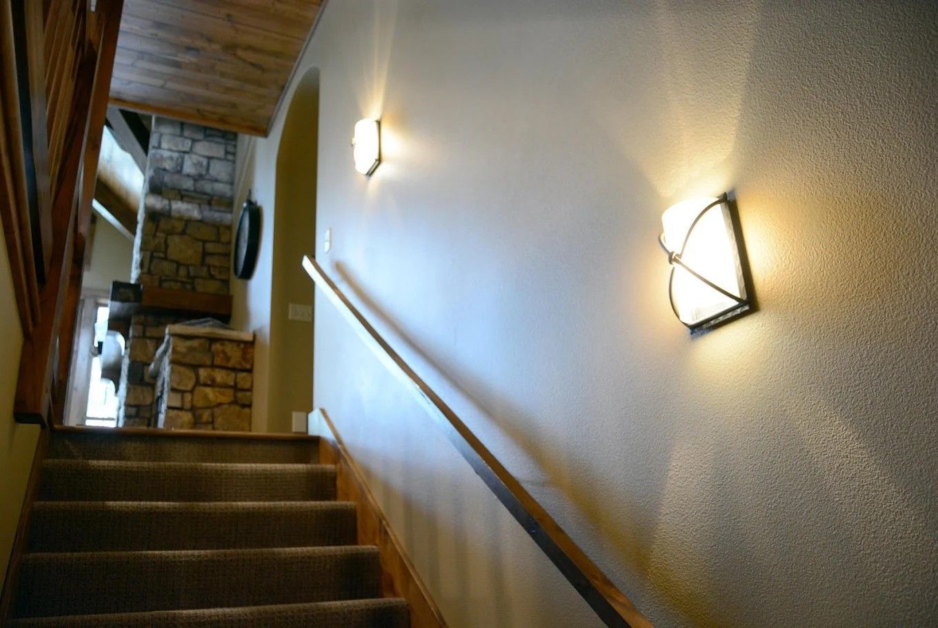 Staircase in a narrow hallway with wall sconces and a wooden handrail.