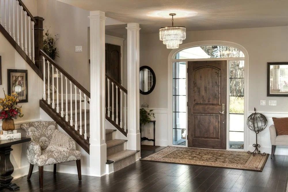Elegant foyer with wood staircase, dark front door, patterned rug, and chandelier