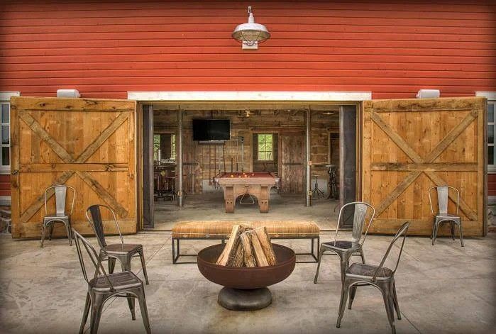 Rustic barn interior with open wooden doors, metal chairs, and a fire pit in front.